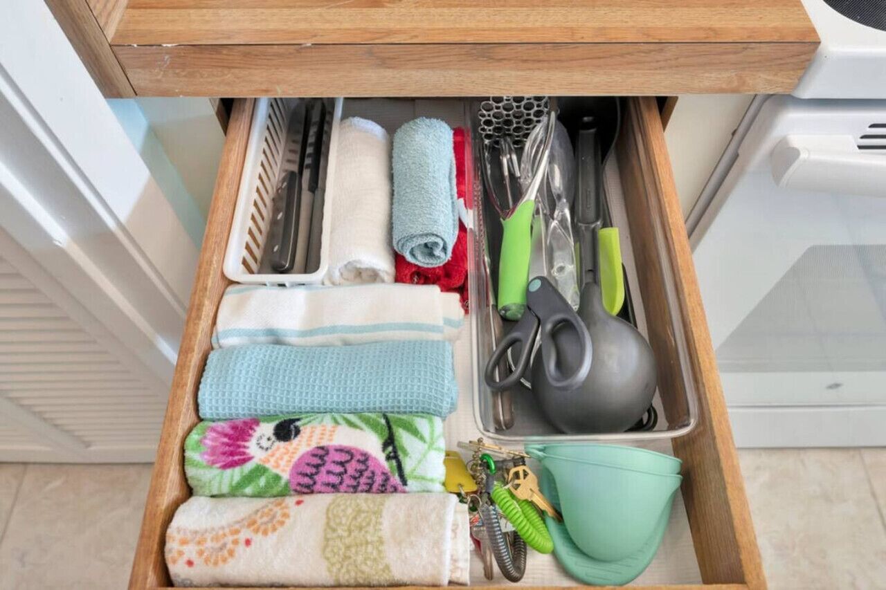 A drawer with neatly organized kitchen utensils, including a green-handled scissor, a black ladle, and a white towel.