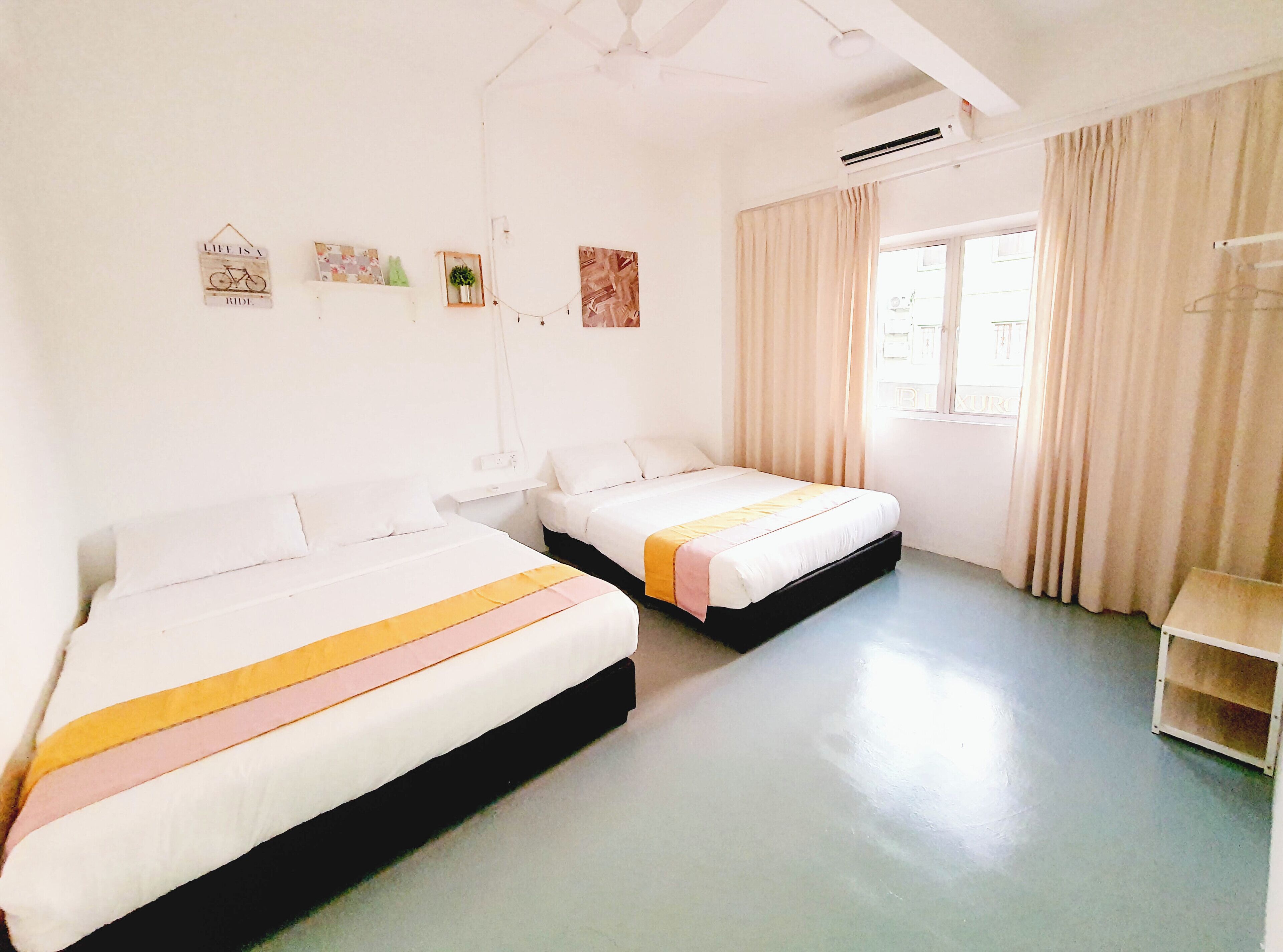 Habitación de hotel limpia y bien iluminada con dos camas individuales, una mesita pequeña y una ventana con cortinas.