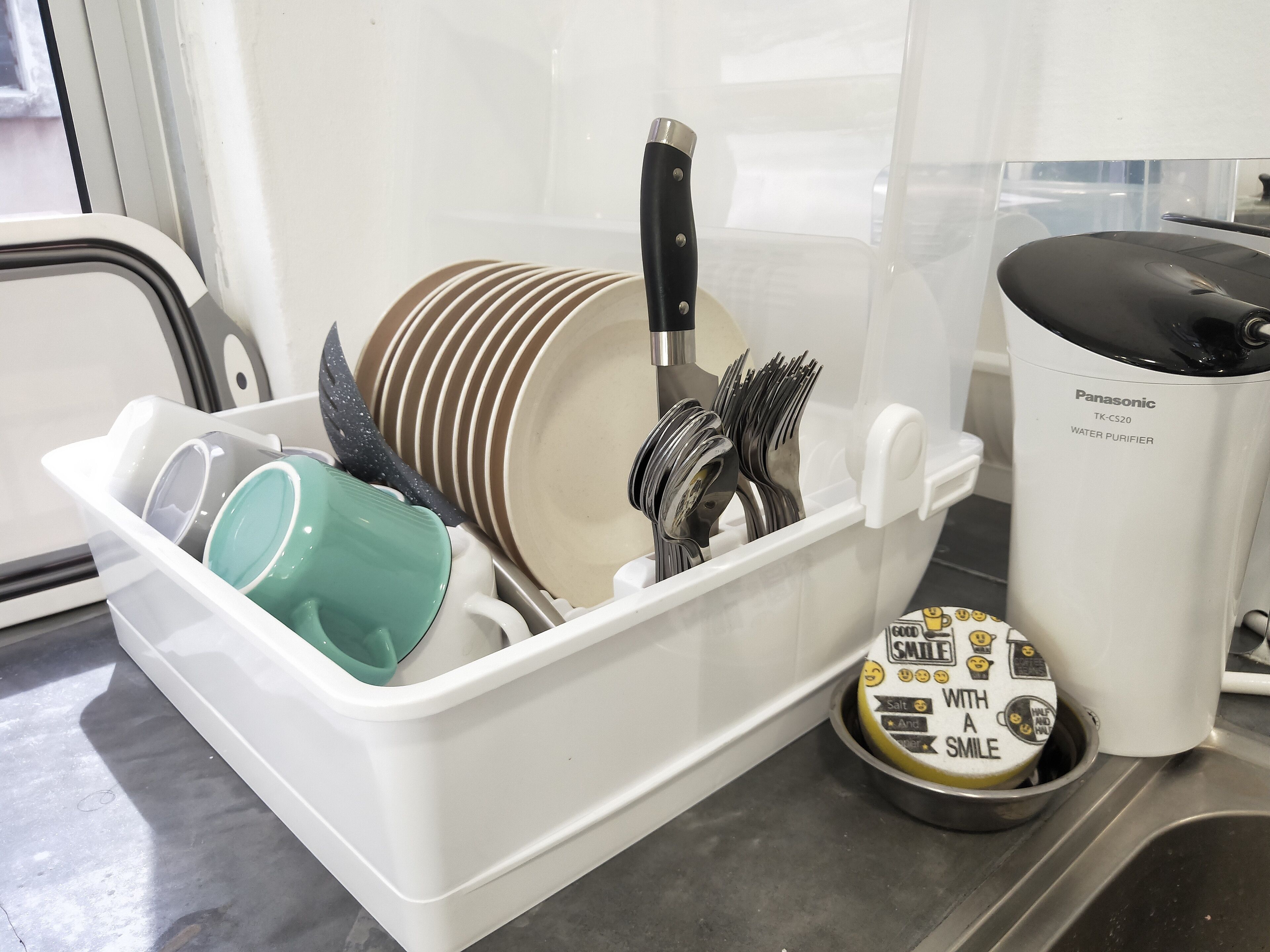 A kitchen with a dish rack holding plates, utensils, and a water purifier.