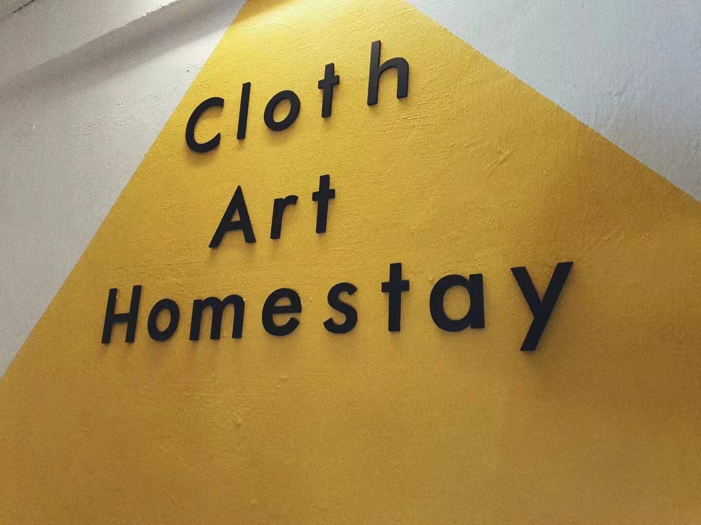 Ein Schild mit dem Schriftzug 'Cloth Art Homestay' auf gelbem und weißem Grund.