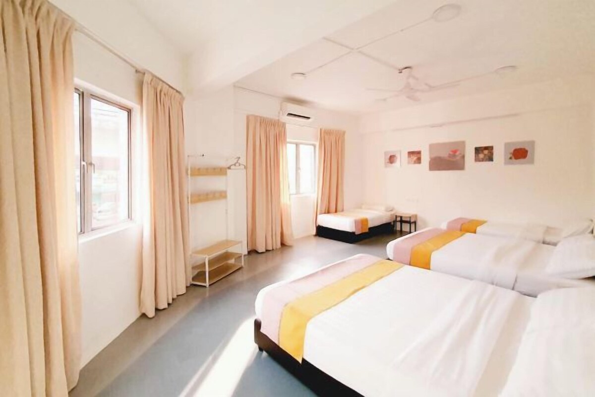 A hotel room with two beds, a window with curtains, a small table, and a wall with pictures.