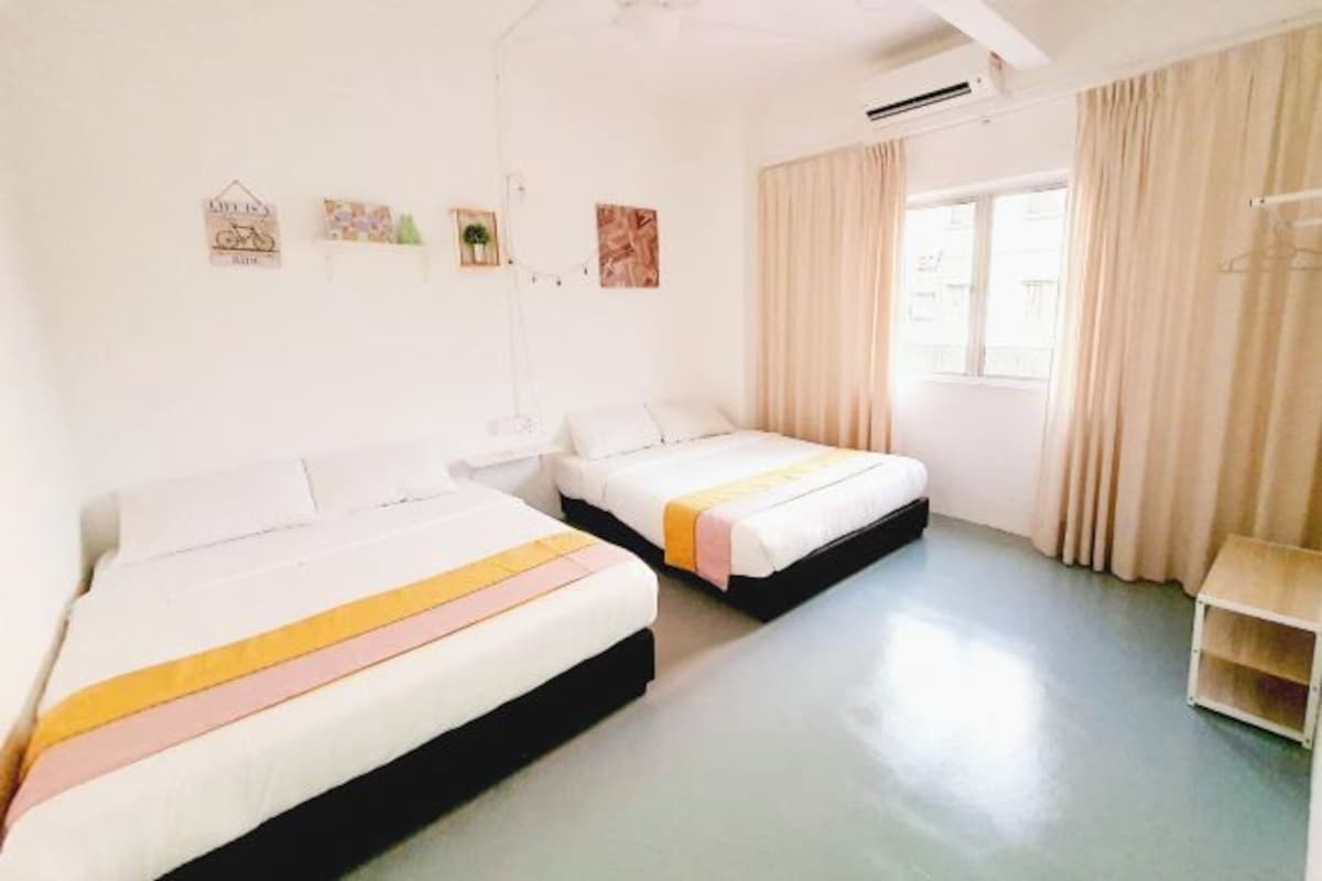 Una habitación con dos camas, una ventana con cortinas y una mesita pequeña.
