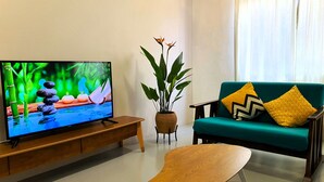 A living room with a television on a wooden stand, a green sofa with patterned cushions, a small wooden table, and a potted plant. - Cloth Art Homestay near Jonker&Pahlawan (Malacca City)
