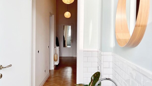 Un couloir avec un plancher en bois, une porte blanche et un miroir fixé au mur.