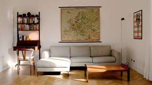 Un salon avec un canapé, une table basse en bois, une bibliothèque et une carte accrochée au mur.