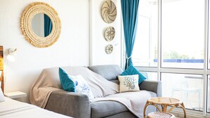 A modern living room with a grey sofa, blue and white cushions, a round mirror, and decorative wall art. - Cosy studio, beach access (Le Gosier)