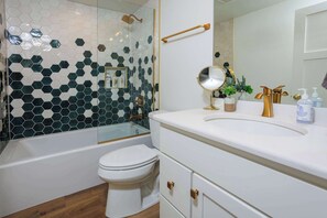 Een badkamer met een wit toilet, een bad, een douche en een wastafel met spiegel en toiletartikelen.