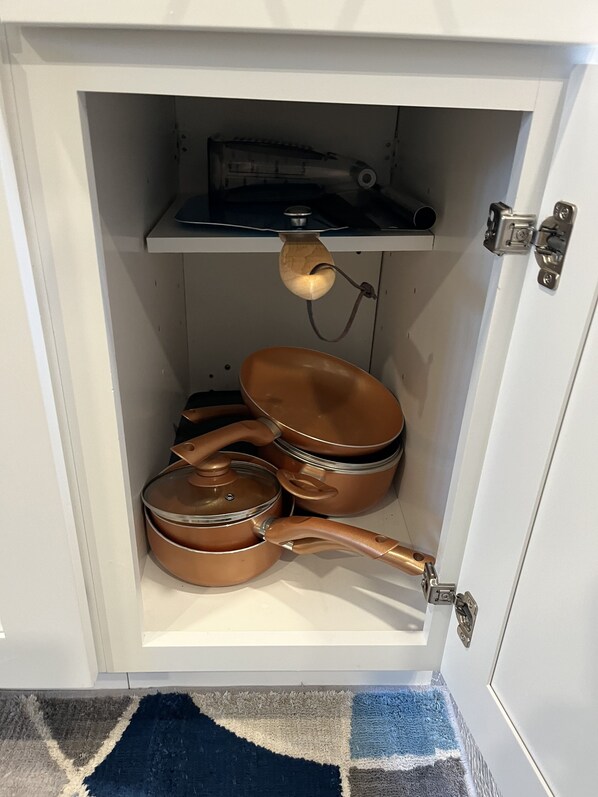Un mueble de cocina con utensilios de cocina de cobre y una lámpara colgante de madera.
