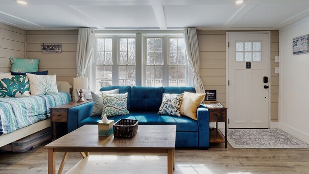 Una sala de estar acogedora con un sofá azul, una mesa de centro de madera y una cama con colcha a rayas.