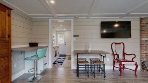 Una cocina moderna con una barra de madera, un taburete de color verde azulado, una silla roja y un televisor montado en la pared.