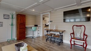 Una cocina compacta con armarios de madera, un comedor con mesa y bancos de madera, una silla roja y un televisor montado en la pared.