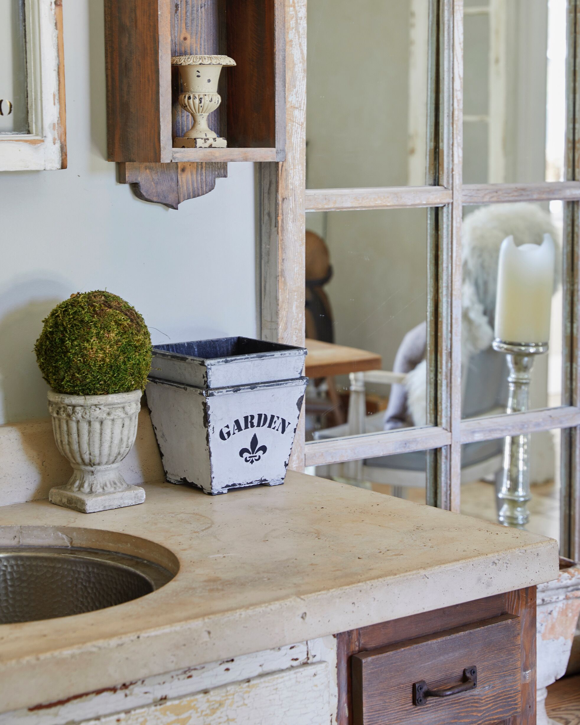 Une cuisine rustique avec un évier ancien, une plante en pot et une boîte décorative portant l’inscription « JARDIN ».