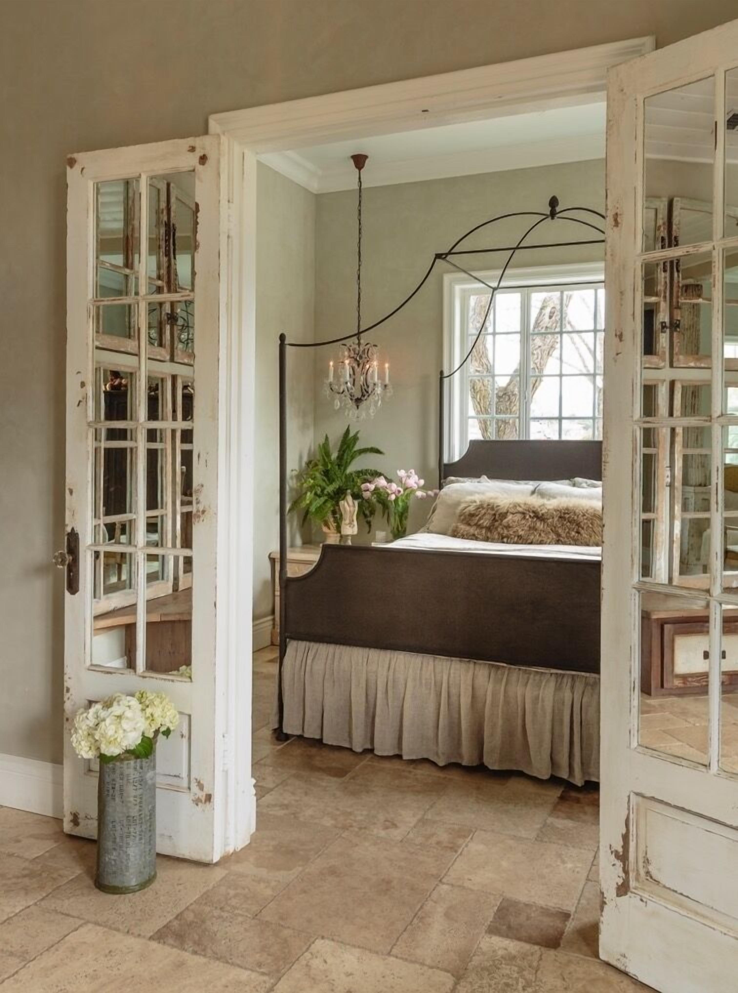 A bedroom with a large bed, a chandelier, and a view through an open door.