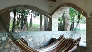 Una hamaca colgada entre arcos de piedra en un espacio al aire libre techado, con suelo de baldosas y techo de madera.
