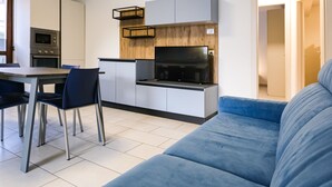 A modern kitchen with built-in appliances, a dining area with chairs, and a blue sofa.