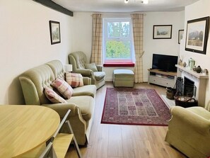 A living room with a sofa set, a television, a fireplace, and a window with curtains. - Tranquil retreat in Keswick, Talcomb (Keswick)