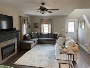 Ein Wohnzimmer mit Ecksofa, Kamin, Fernseher und Deckenventilator.