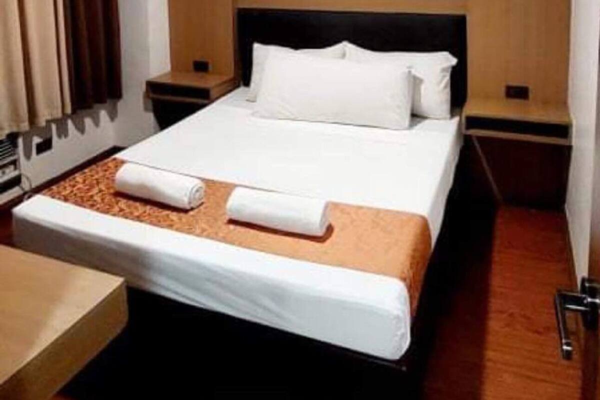 A hotel room with a bed, wooden headboard, nightstands, and a window with curtains.