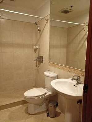 A bathroom with a shower, toilet, sink, and a trash can. - Fernandina 88 Suites Residences (Quezon City)