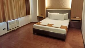 A hotel room with a large bed, a headboard with integrated lighting, a bedside table, and a wall-mounted air conditioning unit. - Fernandina 88 Suites Residences (Quezon City)