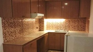 A compact kitchen with wooden cabinets, a tiled backsplash, and a white refrigerator. - Fernandina 88 Suites Residences (Quezon City)