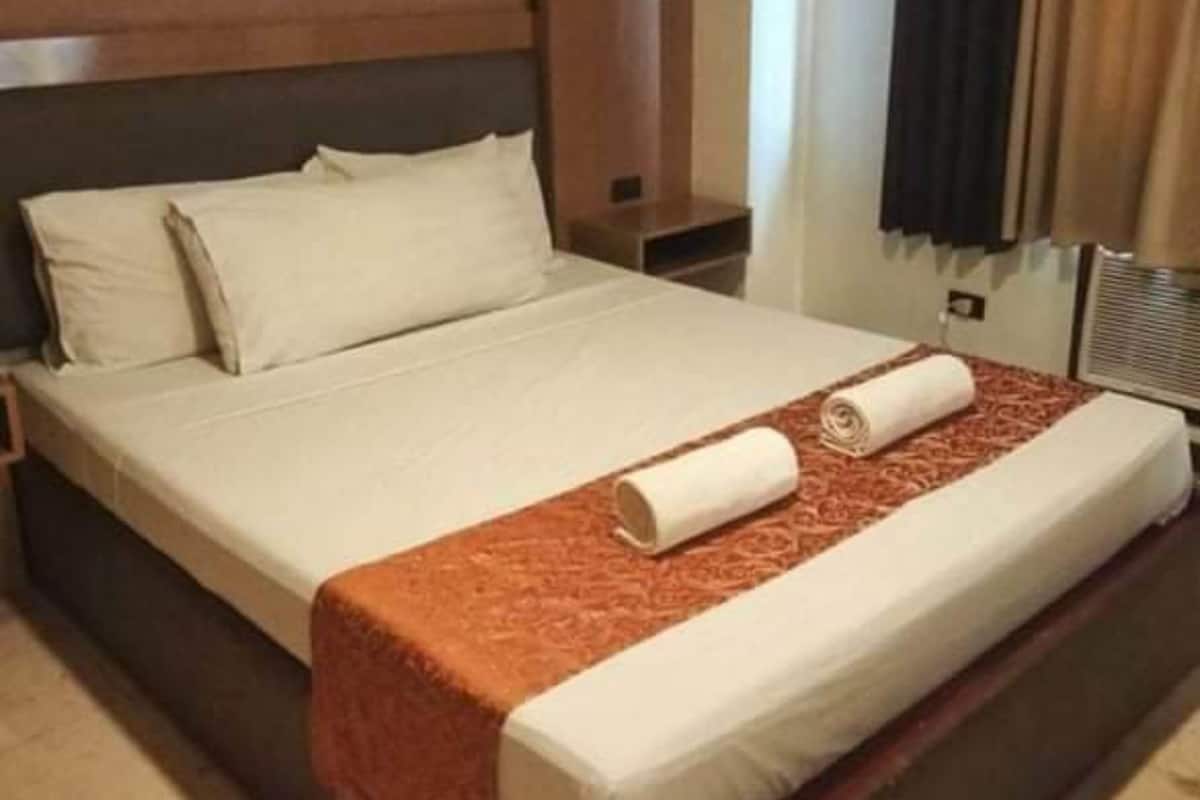 A hotel room with a large bed, a wooden headboard, and a window with curtains.