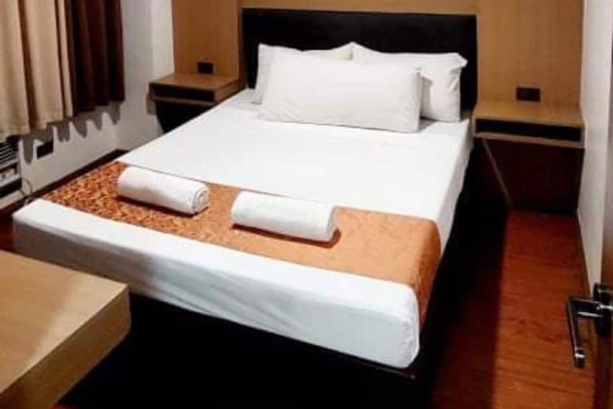 A hotel room with a bed, a nightstand, a wooden bench, and a window with curtains.