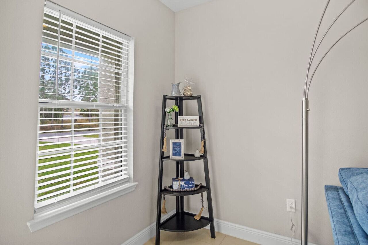 A corner room with a window, a black shelf with decorative items, and a blue towel on the floor.
