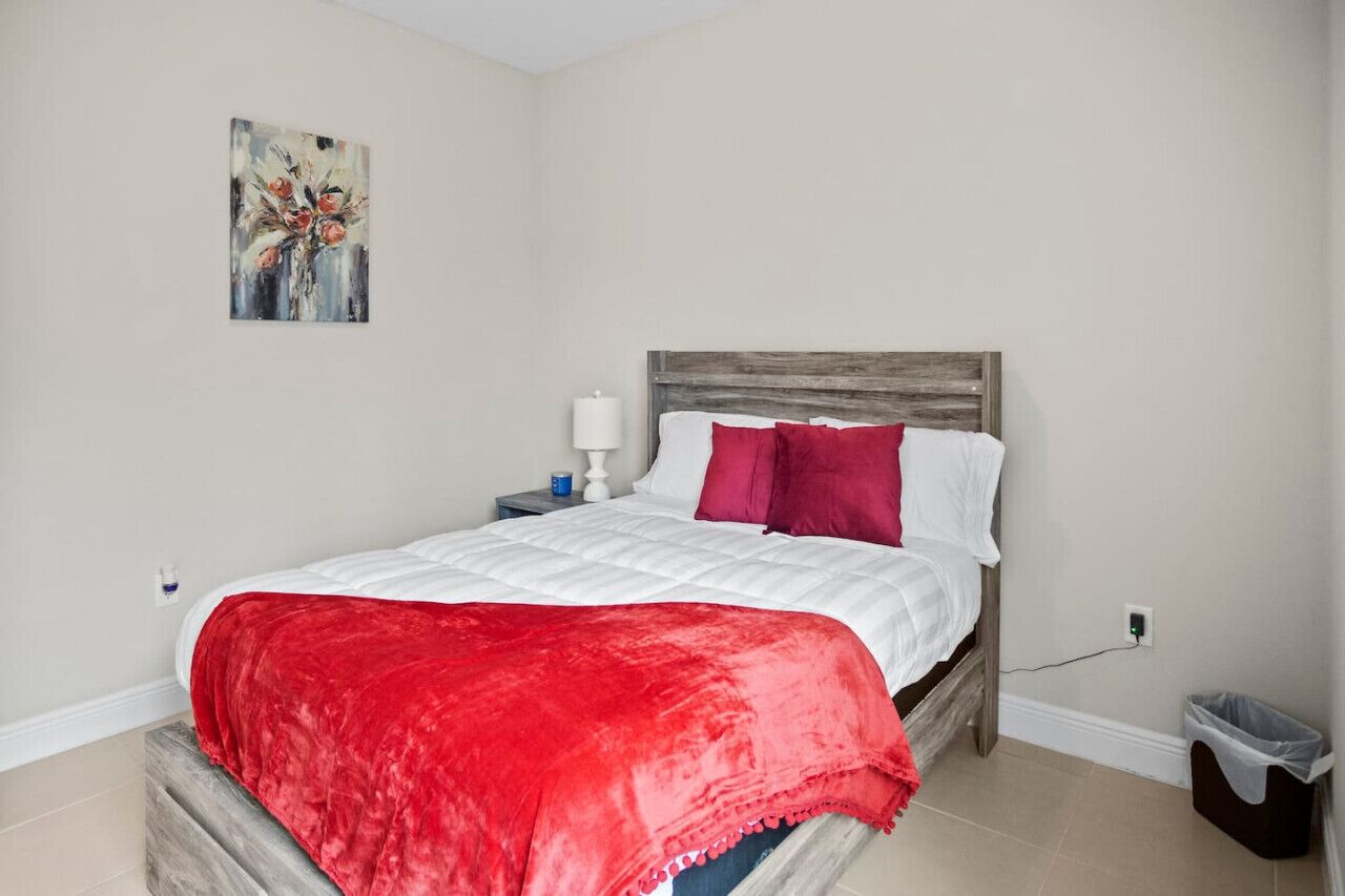 A bedroom with a bed, a nightstand, a lamp, a trash bin, and a painting on the wall.