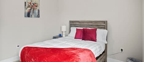 A bedroom with a bed, a nightstand, a lamp, a trash bin, and a painting on the wall.
