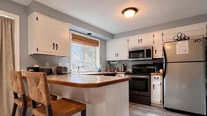 Eine Küche mit Kochinsel, Barhocker, Mikrowelle, Backofen und Kühlschrank.