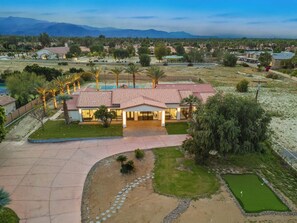 A large house with a spacious driveway, a well-maintained lawn, and a small putting green.