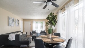 Ein modernes Wohnzimmer mit einem dunkelgrauen Sofa, einem runden Esstisch mit Stühlen und einem Deckenventilator.