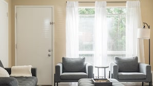 Ein Wohnzimmer mit einem grauen Sofa, zwei Sesseln, einem Couchtisch und einer Tür.