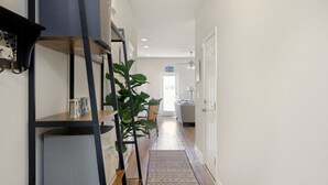 A hallway with a built-in shelf unit, a potted plant, and a rug leading to a door. - Modern 3BR Townhome | Pool Access | Near Publix Sports Park & Beaches | Sleeps 9 (Panama City Beach)