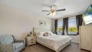 A bedroom with a bed, a nightstand, a chair, a ceiling fan, and a window with curtains. - Modern 3BR Townhome | Pool Access | Near Publix Sports Park & Beaches | Sleeps 9 (Panama City Beach)