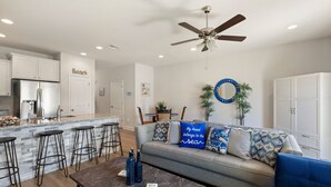 A modern kitchen with a bar area, a dining table, and a living area with a sofa and a coffee table. - Modern 3BR Townhome | Pool Access | Near Publix Sports Park & Beaches | Sleeps 9 (Panama City Beach)