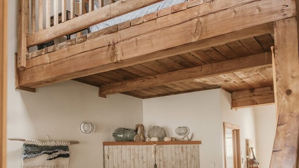 Une pièce de style « loft », avec un escalier en bois, un canapé, un fauteuil et une table à manger.