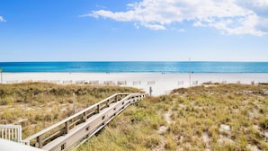 Une plage avec une promenade en bois menant au rivage, une plage de sable et un ciel bleu dégagé.