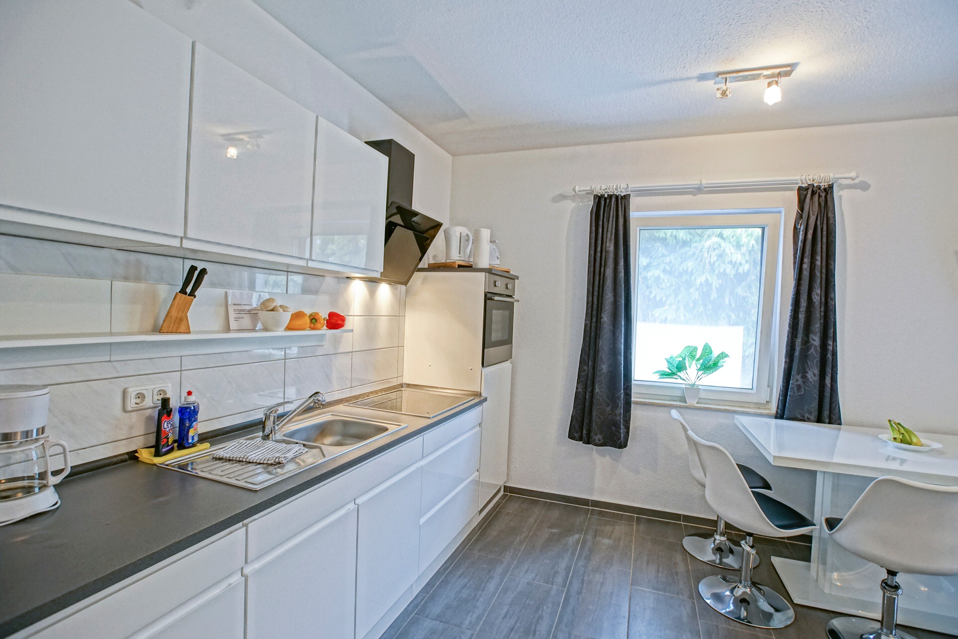 A modern kitchen with white cabinets, a sink, and a dining area with a table and chairs.