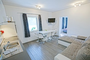 A modern kitchen with a sink, a dining table with chairs, a sofa, and a television mounted on the wall. - Holiday Home 'Ostseeferienhaus Nebengebäude' with Private Terrace and Wi-Fi (Mönkebude)