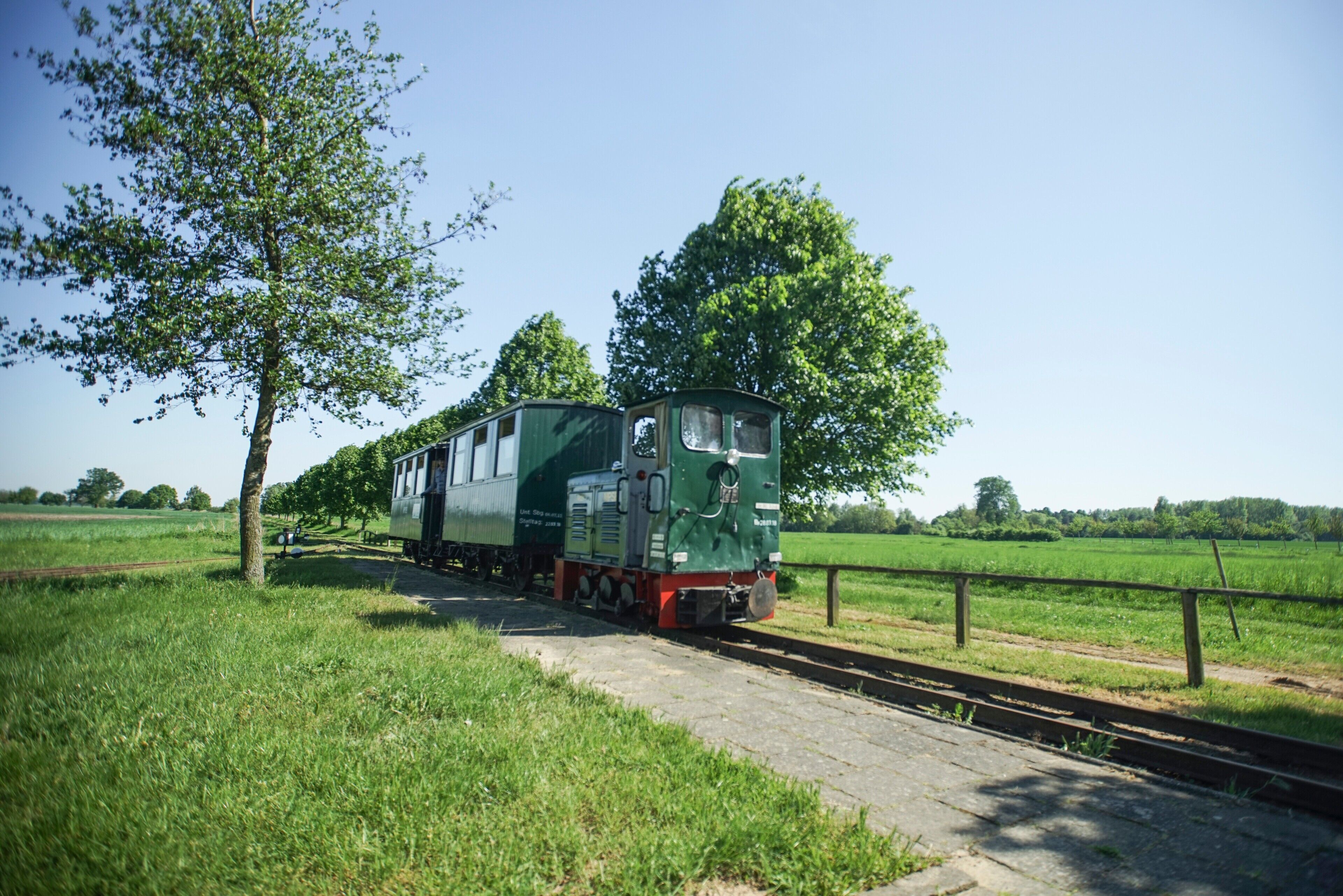 A green train on a railway track in a rural area with trees and open fields.