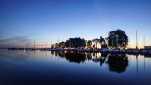 Ein Yachthafen im Abenddämmerung mit ruhigem Wasser, das Boote und Bäume spiegelt, und einem klaren Himmel darüber.