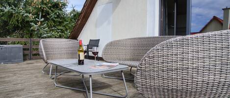 An outdoor patio with wicker furniture, a table with a bottle and glass, and a satellite dish on the wall.