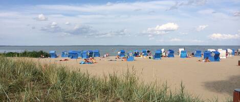 Ein Strand mit Reihen blauer Strandhütten und einem Sandbereich, auf dem sich Menschen befinden.