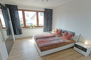 Une chambre avec un grand lit, une table de chevet, une fenêtre avec des rideaux et un radiateur.
