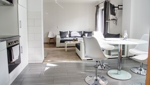 Une cuisine moderne avec des armoires blanches, un four encastré et un coin repas comprenant une table en verre et des chaises blanches.