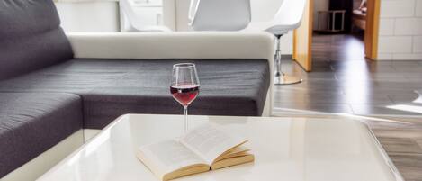 A modern living room with a sofa, a coffee table with a book and a glass of red wine, and a white chair.