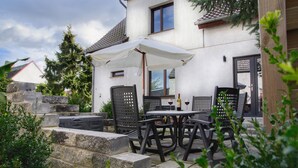 Une terrasse avec des meubles d’extérieur, un parasol blanc et un mur en pierre.
