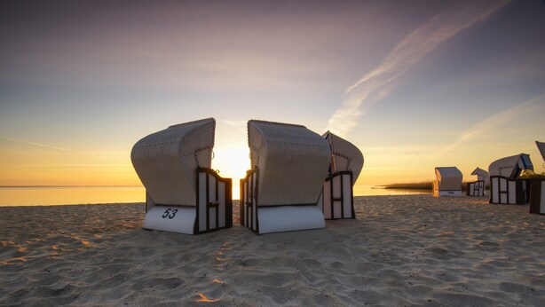 Une plage avec des chaises longues en osier et le chiffre « 53 » peint sur le sol.
